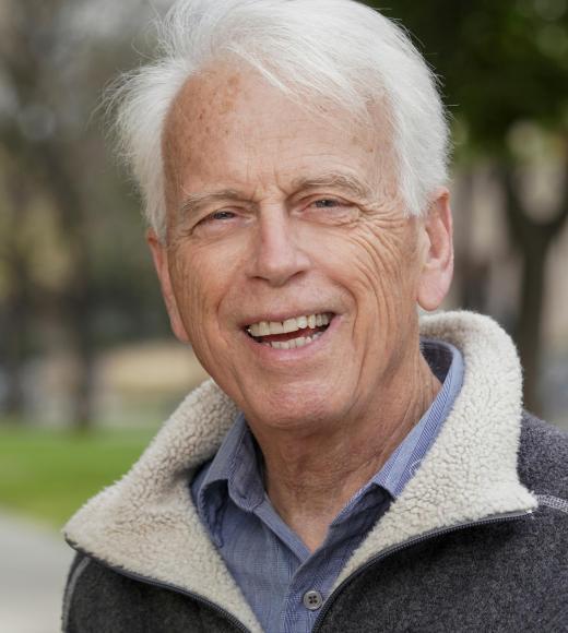 Smiling older man with white hair in gray fleece jacket, outdoor portrait
