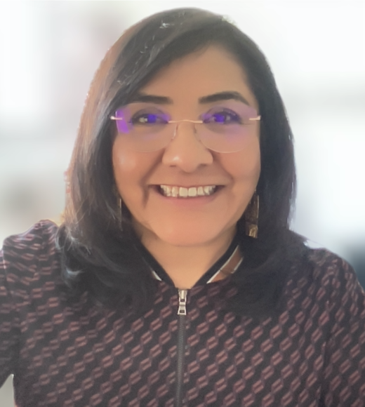 Smiling woman with dark hair, glasses and patterned zip jacket, blurred background photograph