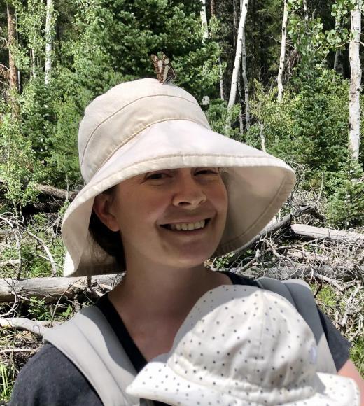 Woman in wide-brim hat smiling while holding baby in dotted hat, forest background, photo
