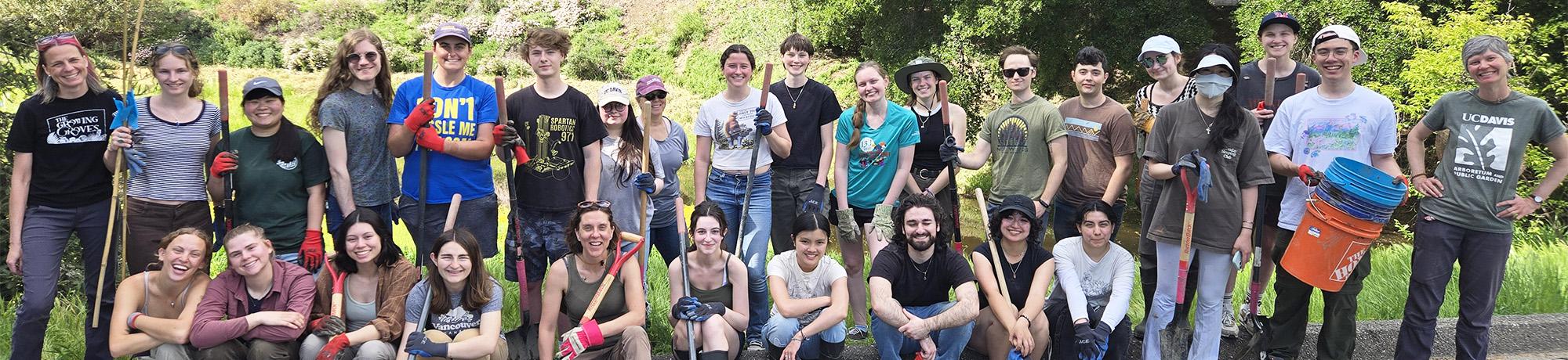 Diverse group of people posing on grass in a sunny park with trees behind